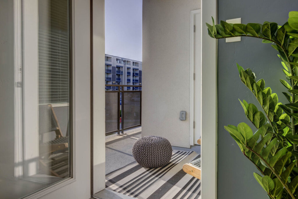 Apartment balcony view from inside apartment, decorative small grey bean bag in the middle of the floor on top of a rug