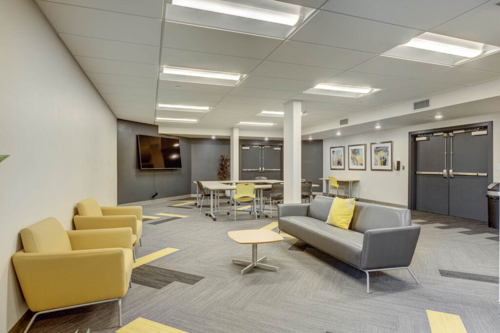 The inside of the clubhouse featuring grey couches and yellow cushioned chairs with yellow accent pillows for residents to relax and socialize.