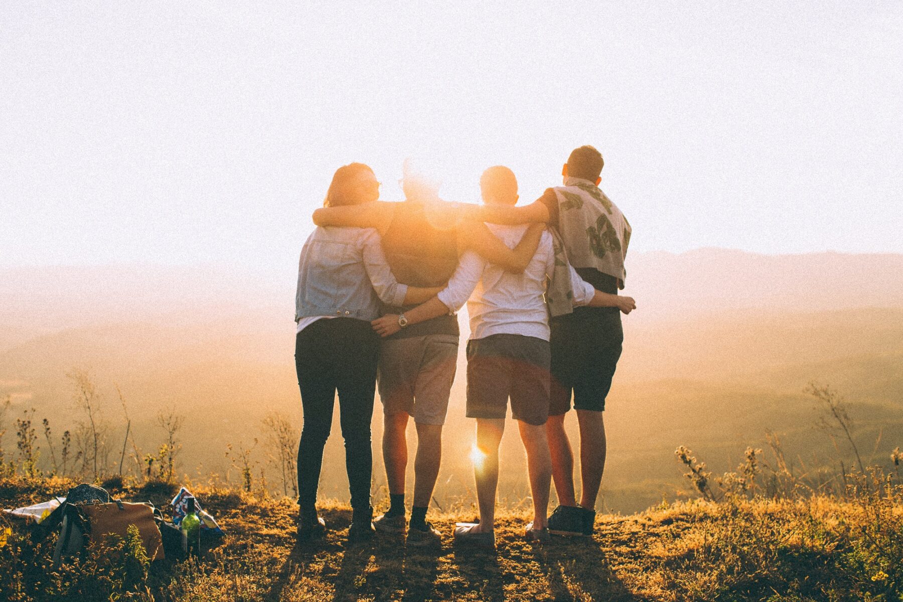 group of four friends standing outside overlooking mountains embracing each other